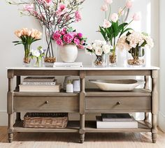 a table with flowers and vases on it in front of a wall mounted mirror