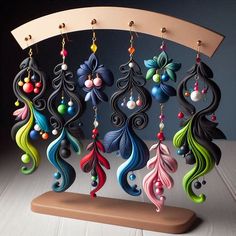 an assortment of colorful earrings hanging from hooks on a wooden stand in front of a dark background