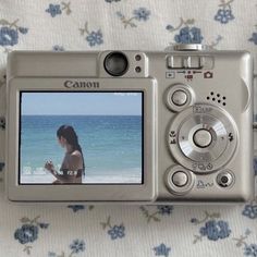 a digital camera sitting on top of a bed next to a flowered sheet with the image of a woman