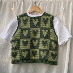 a green and black sweater vest hanging on a white wall next to a wooden hanger