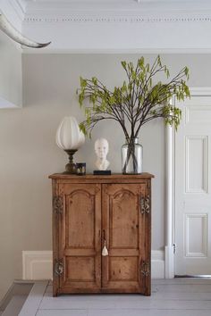 a wooden cabinet with two vases on top of it and a plant next to it