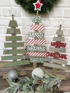 three wooden christmas trees sitting on top of a table next to a wreath and other decorations