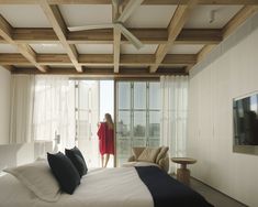 a woman in a red robe is standing near a bed with white sheets and pillows