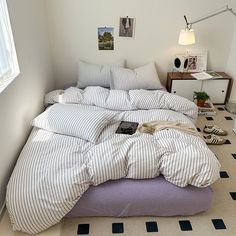 an unmade bed sitting in a bedroom next to a lamp and pictures on the wall