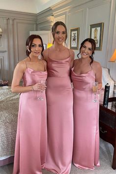 three women in pink dresses standing next to each other holding wine glasses and posing for the camera