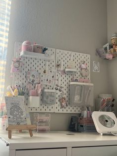 a white desk topped with lots of clutter next to a wall mounted pegboard