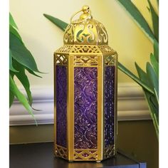 a purple and gold lantern sitting on top of a table next to a potted plant