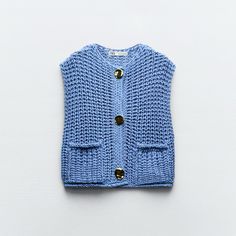 a blue knitted sweater with buttons on the front and back, sitting on a white surface