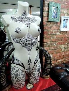 a white mannequin with black designs on it's chest and arms, in front of a brick wall