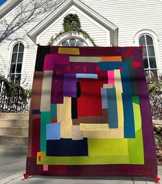 a colorful quilt hanging from the side of a white church