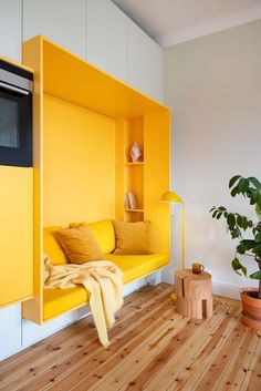 a yellow couch sitting on top of a wooden floor next to a potted plant