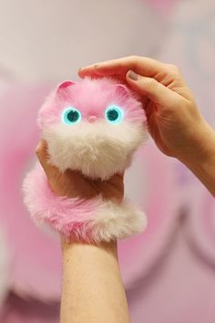 a person holding up a pink and white stuffed animal with blue eyes on it's face