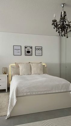 a bedroom with a white bed and chandelier in the corner, along with pictures on the wall