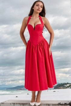 a woman in a red dress is standing on a ledge near the ocean with her hands on her hips