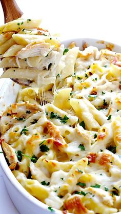 a wooden spoon scooping some pasta from a casserole dish with chicken and cheese