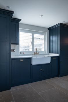 a kitchen with dark blue cabinets and white sink in the center, along with tile flooring