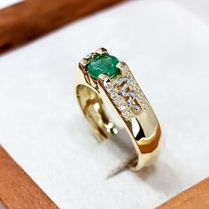 a gold ring with an emerald and diamond set in the middle, sitting on top of a wooden box