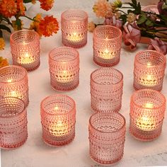 many pink glass candles are lit on a table