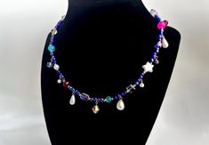 This quirky handmade necklace combines iridescent seed beads, and various other beads in shades like neon pink, turquouse, raspberry red, lavender purple, and royal blue to create a unique piece. This necklace isn't for the faint of heart, but those who like to stand out, and add a little off-beat color to their look. Oblong pearl charms in different shapes hang from the necklace, as well as other pearl and crystal beads, adding other intriguing bits to the necklace. Necklace is secured in the back with a lobster clasp hook, but can be adjusted fora looser fit. Handmade Dangle Charm Necklaces For Parties, Dainty Handmade Beaded Necklaces For Party, Handmade Dainty Beaded Necklace For Party, Dainty Handmade Beaded Necklace For Party, Iridescent Necklaces With Colorful Beads For Gifts, Iridescent Necklaces With Colorful Beads As A Gift, Iridescent Necklace With Colorful Beads For Gift, Red Lavender, Raspberry Red