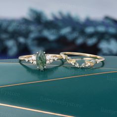 two gold rings with green and white stones sitting on top of a blue table next to each other