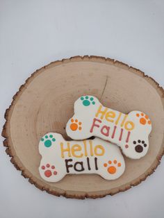 two decorated cookies sitting on top of a piece of wood with the words hello fall written on them