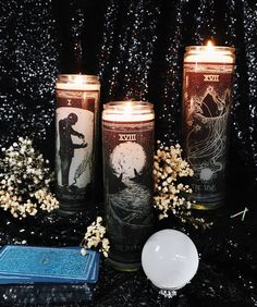 three candles are sitting next to each other on a black table with flowers and an object