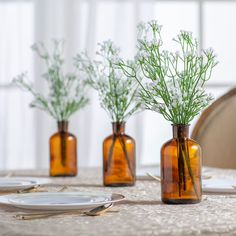 three brown glass vases with plants in them sitting on a table set for dinner