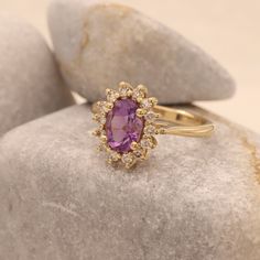 an oval shaped pink sapphire and diamond ring sitting on top of a rock next to some rocks