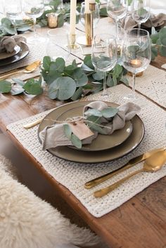 the table is set with plates, silverware and greenery