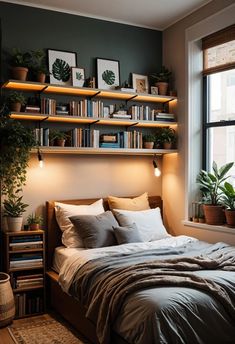 a bed sitting under a window next to a wooden shelf filled with books and plants