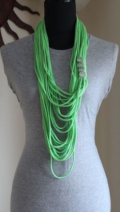 a woman wearing a gray shirt and green necklace on top of a mannequin