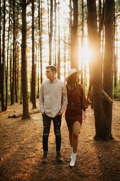 a man and woman are walking through the woods at sunset with sunbeams in the background