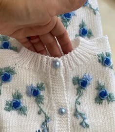 a woman's hand holding onto a white sweater with blue flowers