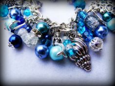 This is a handmade beaded charm bracelet full of wonderful Tibetan silver and silver plated charms, glass beads and pearls inspired by Sirens of the sea. The charms are sea shells, mermaids, turtles, dolphins, starfish and other sea inspired themes with a beautiful dragonfly clasp. This is 7.5 inches long but can be made longer if required :)  In mythology, sirens were seen as beautiful and dangerous creatures depicted as mermaids who used to lure sailors into rocks with their enchanting singing Silver Metal Charm Bracelet With Pearl Charm, Handmade Silver Ocean-inspired Bracelets, Handmade Silver Beaded Bracelets Ocean-inspired, Ocean-inspired Silver Beaded Jewelry, Ocean-inspired Silver Beaded Bracelets, Silver Beaded Ocean-inspired Jewelry, Silver Beaded Ocean-inspired Bracelets, Silver Metal Beaded Bracelet For Beach, Handmade Silver Charm Bracelet For Beach