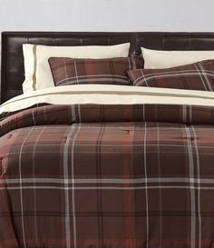 a bed with brown and white plaid comforter set on it's headboard