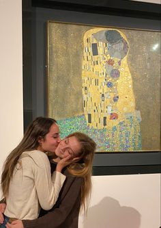 two women are hugging each other in front of a painting on the wall behind them