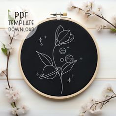 a black and white embroidery pattern on a wooden hoop with cherry blossoms in the background