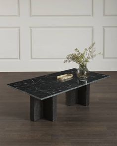 a black marble coffee table with two vases and flowers in it on a hard wood floor