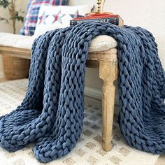 a blue knitted blanket sitting on top of a wooden stool next to a white couch