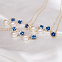 three necklaces with blue stones and pearls on a white cloth, next to a gold chain