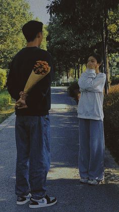 two people standing on the side of a road with one holding a flower and the other covering his mouth