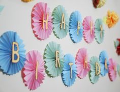 colorful paper fans with the words happy birthday written on them are hanging from a wall