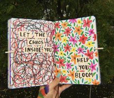 a hand holding up an open notebook with writing on the pages and flowers painted on it