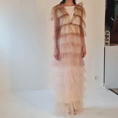 a woman standing in front of a white wall wearing a dress with ruffles