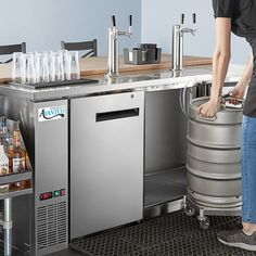 a woman standing next to a metal keg filled with bottles and glasses on top of a counter