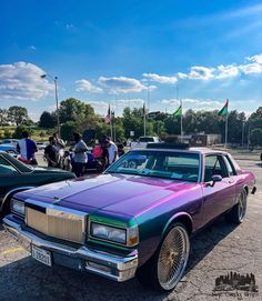 a purple car parked in a parking lot next to other cars and people standing around