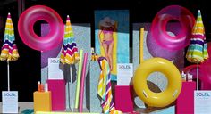 an assortment of beach accessories on display in front of a store window with pink and yellow umbrellas