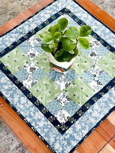 a potted plant sitting on top of a wooden table next to a blue and green quilt