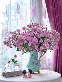 a vase filled with pink flowers sitting on top of a table next to a couple figurines