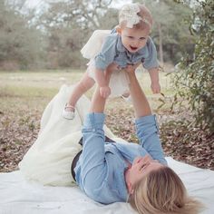 a woman laying on top of a white blanket holding a baby up in the air